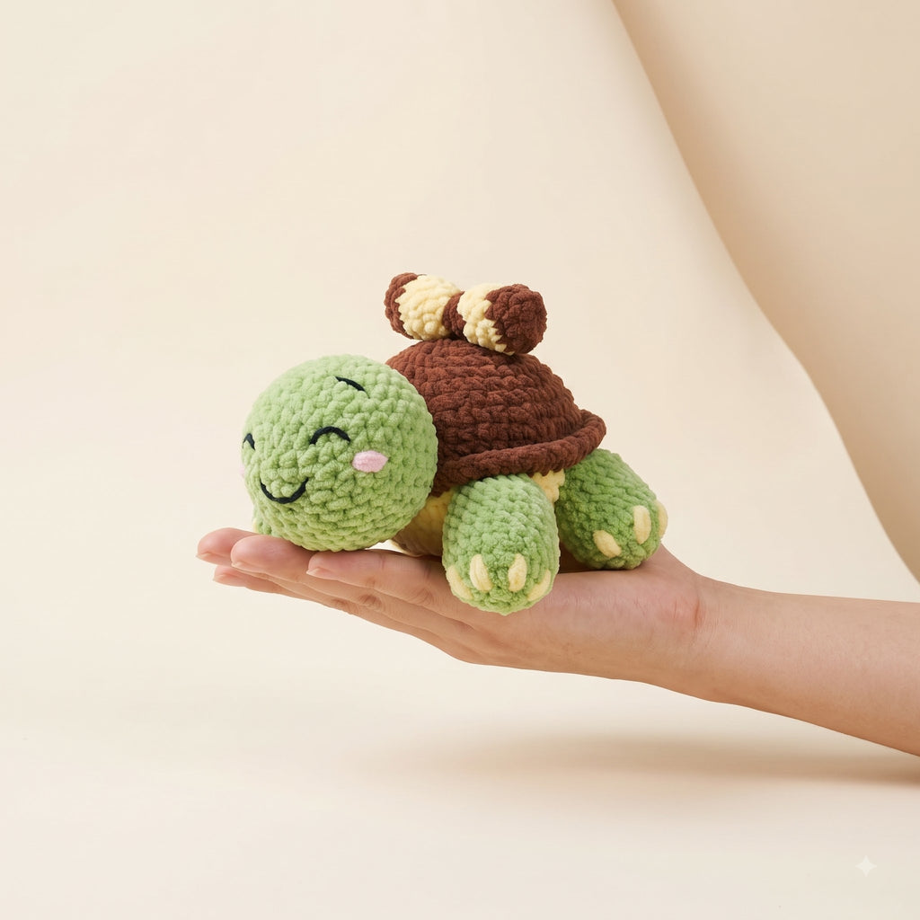 A small crocheted turtle plush toy being held in a person's hand against a soft beige studio background.