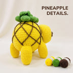 A crocheted pineapple-shaped plush toy shown from the back on a white studio background, with the text 'PINEAPPLE DETAILS.' above it and three yarn balls in yellow, green, and brown at the lower right.