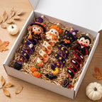 A gift box filled with crocheted Halloween stockings and small seasonal charms, displayed on a wooden surface with pumpkins and autumn leaves around it.