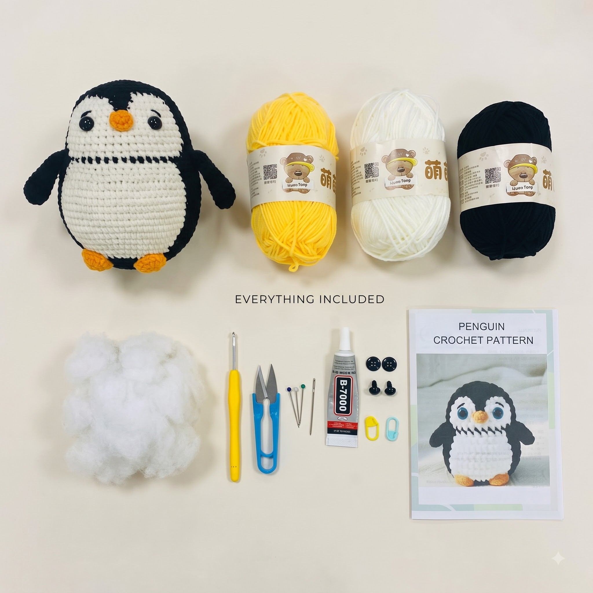 Crochet penguin kit laid out on a light beige background, including a crocheted penguin, balls of yarn in black, white, and yellow, stuffing, crochet hook, scissors, pins, glue, buttons, and a penguin crochet pattern booklet.