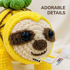 A close-up of a crocheted sloth toy wearing a yellow hood with a green leafy top, shown against a soft cream background. The text 'ADORABLE DETAILS' appears in the upper right, and small crafting accessories are visible near the bottom right.