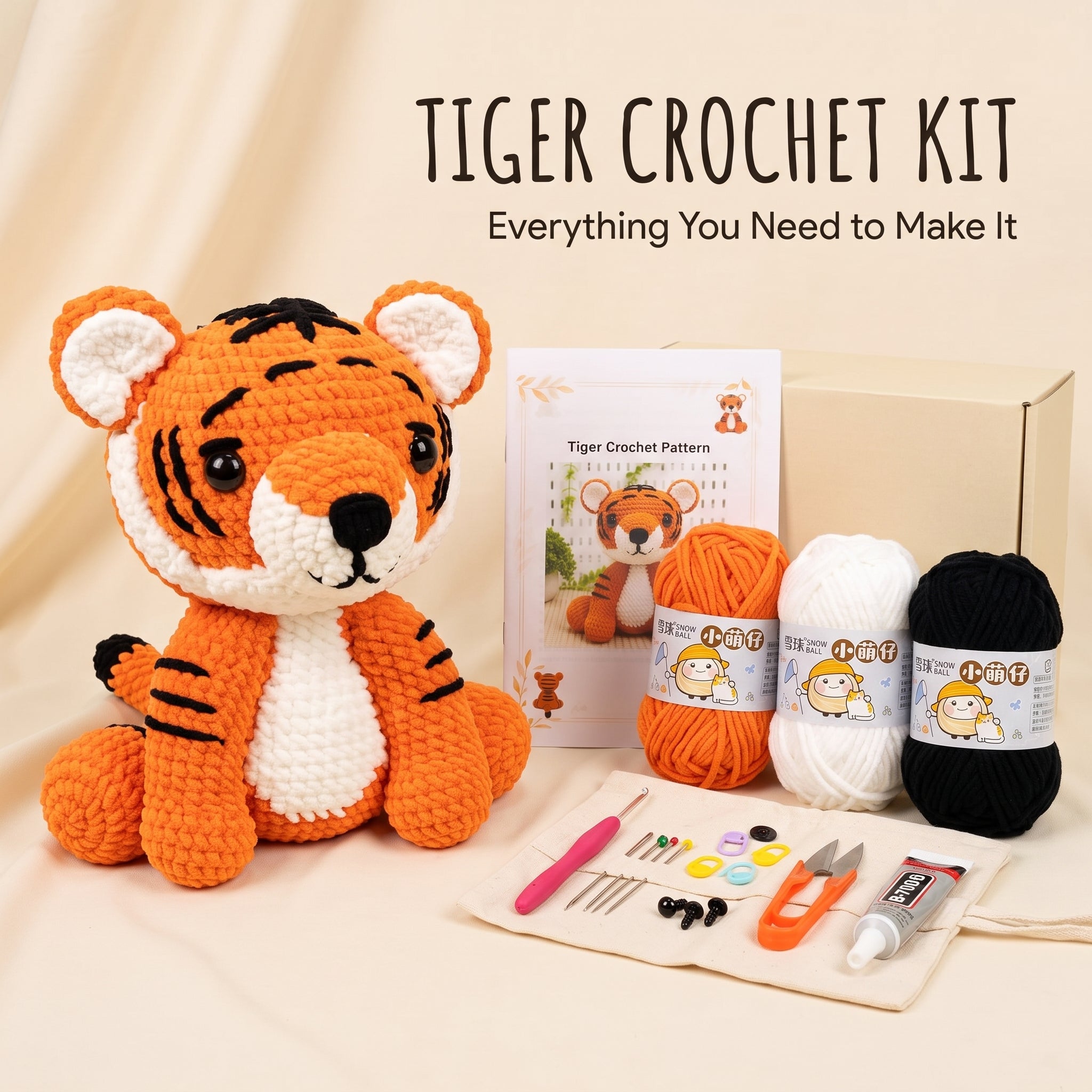Tiger crochet kit displayed on a beige fabric background, featuring a crocheted tiger plush, a pattern booklet, a cardboard box, orange and white yarn balls, black yarn, crochet hooks, thread, scissors, and other small crafting tools. Text at the top reads 'TIGER CROCHET KIT' and 'Everything You Need to Make It'.