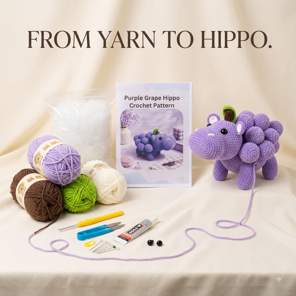 Crochet pattern kit for making a purple grape hippo amigurumi toy, displayed on a beige fabric background. The kit includes a book titled 'Purple Grape Hippo Crochet Pattern', purple, lavender, brown, green, and cream yarn balls, crochet hooks, a needle threader, a glue tube, and a completed purple hippo toy with its yarn tail attached.