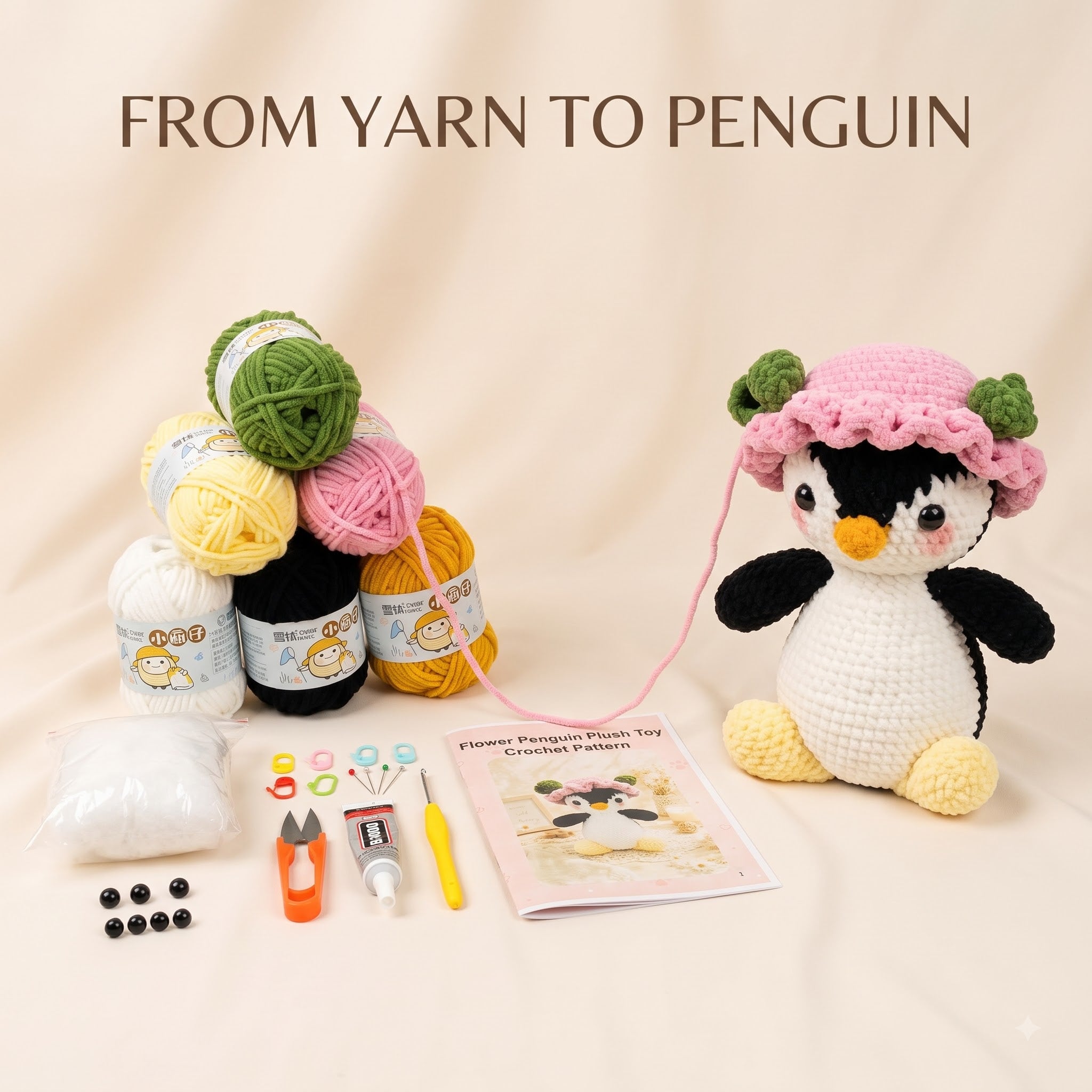 A crocheted penguin toy kit displayed on a beige fabric background with the text 'FROM YARN TO PENGUIN'. The main product is a white and black crocheted penguin wearing a pink and green hat, alongside various yarn balls in green, yellow, pink, black, and white, beads, thread, a small knife, and a pattern booklet.