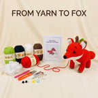 Crochet kit titled 'FROM YARN TO FOX' arranged on a cream fabric backdrop, including a finished red crocheted fox, several balls of yarn, a crochet pattern booklet, needles, thread, scissors, and other crafting tools.