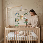 A baby nursery scene with a wooden crib containing a sleeping baby, a woman standing beside the crib, and a wooden baby mobile with hanging duck, frog, dragonfly, and flower toys.