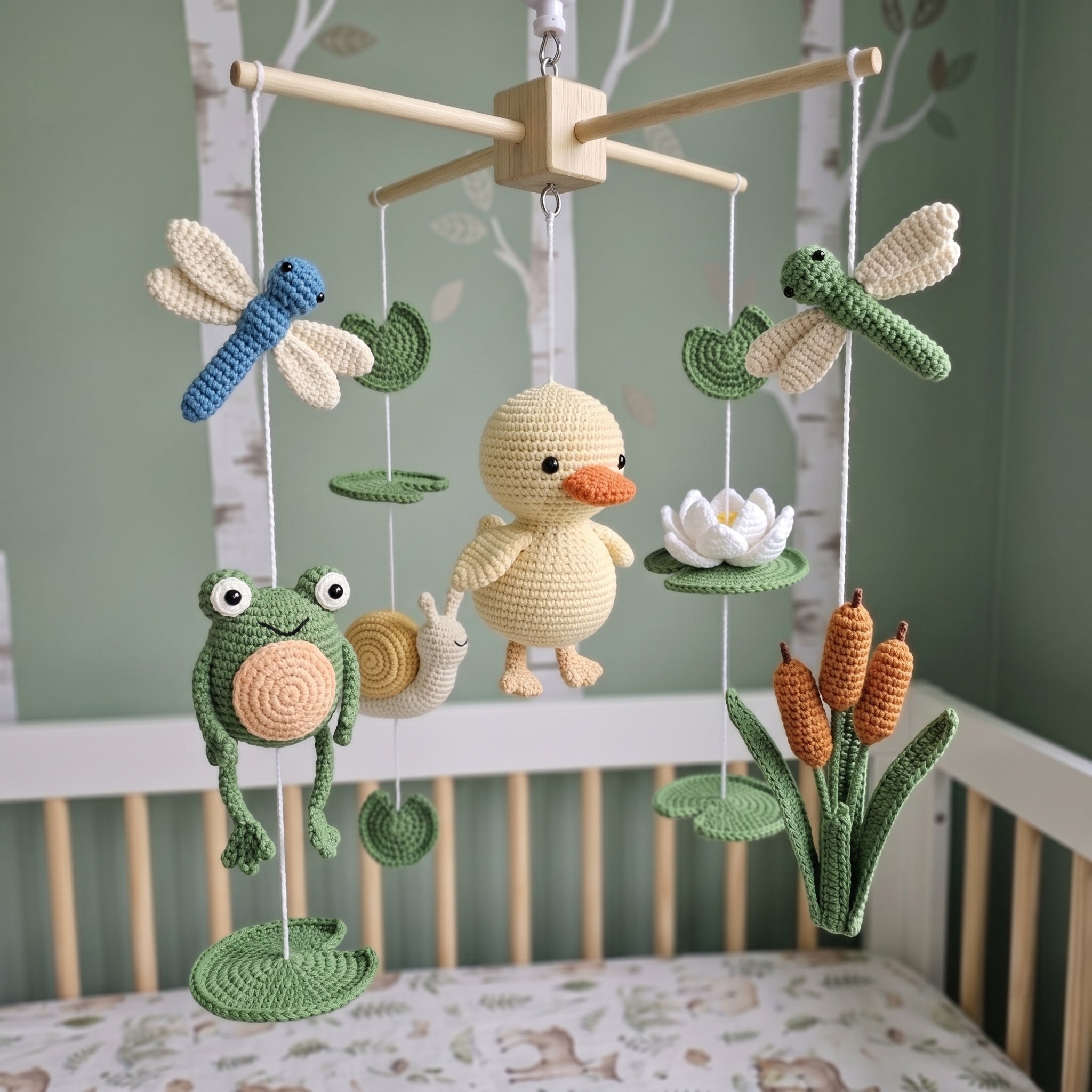 A crocheted baby mobile with a central yellow duck, green frog, blue dragonfly, white lotus, snail, and cattails, hanging above a crib in a nursery.