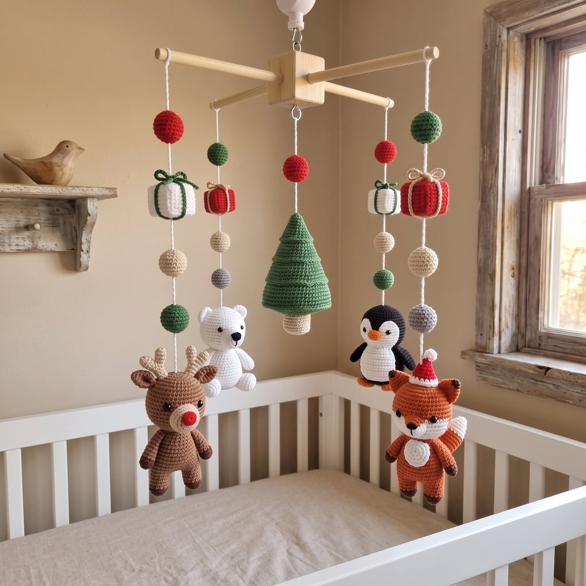 A wooden baby crib in a warm beige nursery, decorated with a hanging crocheted mobile featuring a green Christmas tree, red and white gift boxes, a brown reindeer, a white polar bear, a penguin, and an orange fox.