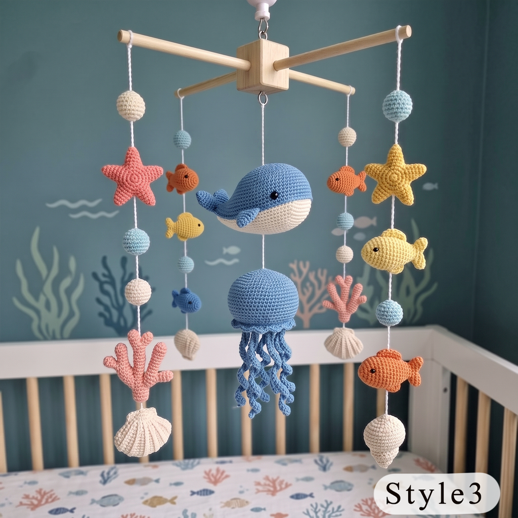 A crocheted baby mobile with ocean-themed toys including a blue whale, octopus, starfish, fish, coral, and shells, hanging above a crib in a blue nursery setting.