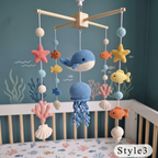 A crocheted baby mobile with ocean-themed toys including a blue whale, octopus, starfish, fish, coral, and shells, hanging above a crib in a blue nursery setting.