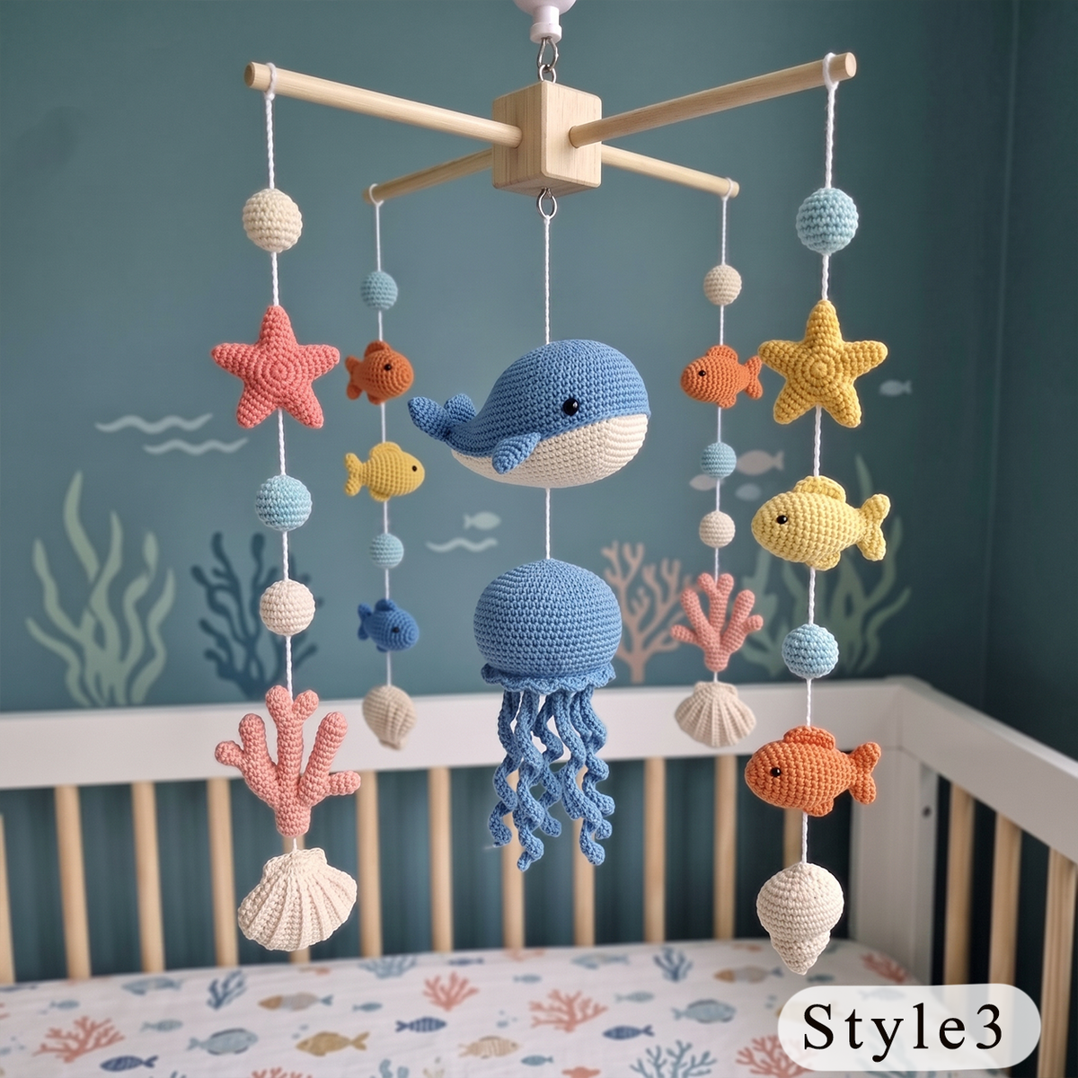 A crocheted baby mobile with ocean-themed toys including a blue whale, octopus, starfish, fish, coral, and shells, hanging above a crib in a blue nursery setting.