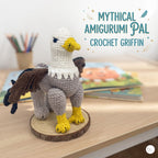 Handmade crocheted Griffin plush with a white head, yellow beak, gray body, yellow claws, and brown wings, standing on a round wood slice base next to text that reads MYTHICAL AMIGURUMI PAL CROCHET GRIFFIN.