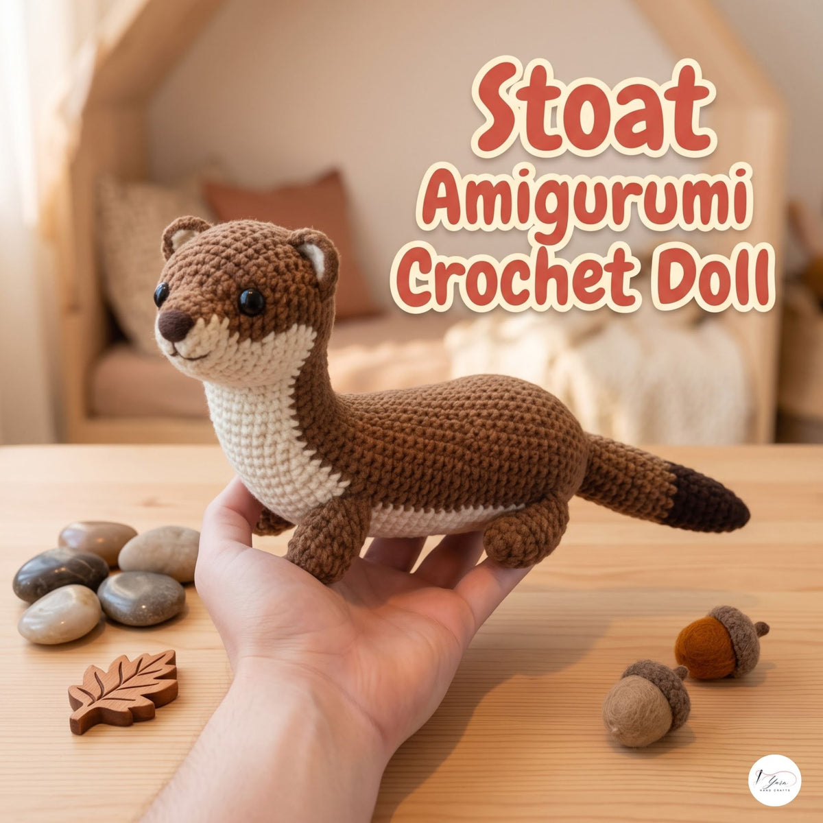 Handmade Stoat crochet amigurumi plush doll in brown and cream with a dark-tipped tail held in a hand on a wooden table, next to small decorative acorns and wooden leaves, with text reading Stoat Amigurumi Crochet Doll.