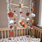A crocheted baby mobile hanging above a wooden crib, featuring autumn-themed elements including maple leaves, acorns, mushrooms, stars, and a crescent moon with a sleeping fox. The crib has an autumn leaf print, and a 'Style2' label is visible in the bottom right corner.