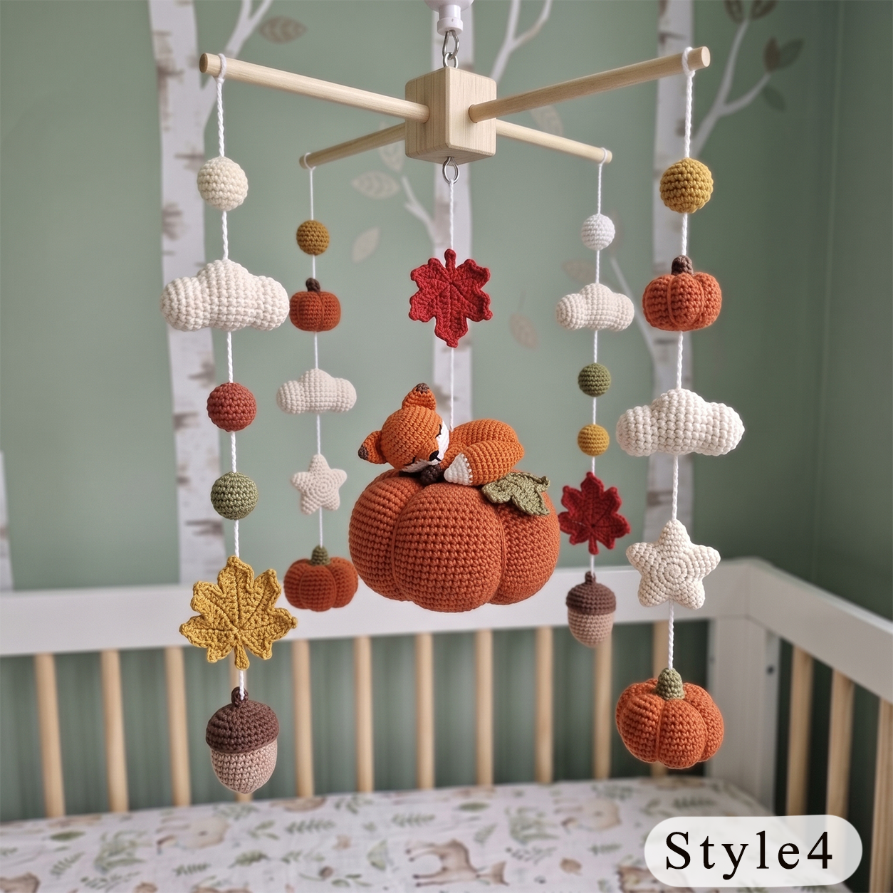 Crocheted autumn-themed baby mobile hanging above a crib, featuring a central pumpkin, acorns, leaves, stars, and a fox, shown in a nursery setting.
