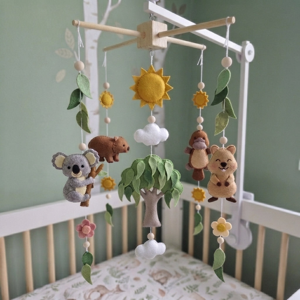 A felt baby mobile with woodland animals and a tree, hanging in a white crib against a sage green wall.