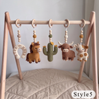 A wooden baby activity gym with five crocheted hanging toys: a horseshoe, horse, cactus, bull, and cow, displayed on a beige quilted floor against a light gray wall.