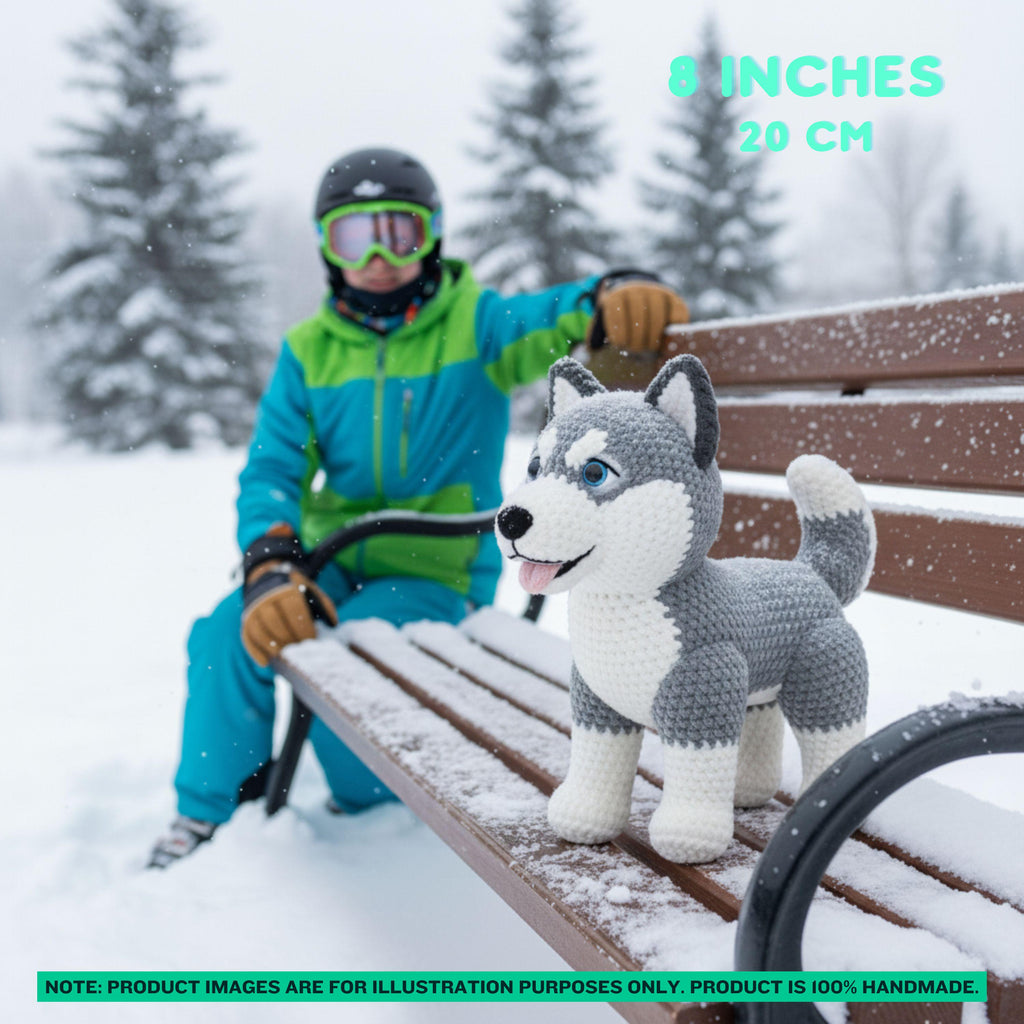 A crocheted husky dog toy sits on a snow-covered wooden bench in a snowy outdoor setting, with a person in ski gear seated behind it. Text overlays indicate the size as 8 inches / 20 cm.