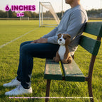 A person sitting on a green wooden bench on a grassy soccer field, holding a small brown and white crocheted dog toy. Text overlays indicate the toy is 6 inches (15 cm) and note that the product image is for illustration purposes only.