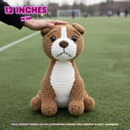 A brown and white crocheted dog plush toy sits on a green sports field, with a human hand resting on its head. Text overlays indicate the size is 12 inches (30 cm) and note that the product image is for illustration purposes only.