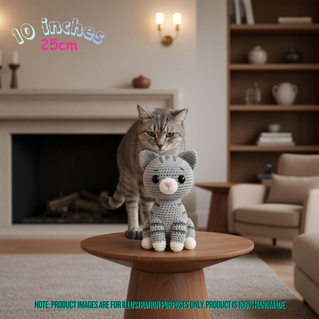 Handmade 10 inches 25cm grey tabby cat crochet amigurumi plush doll sitting next to a real tabby cat in front of a fireplace
