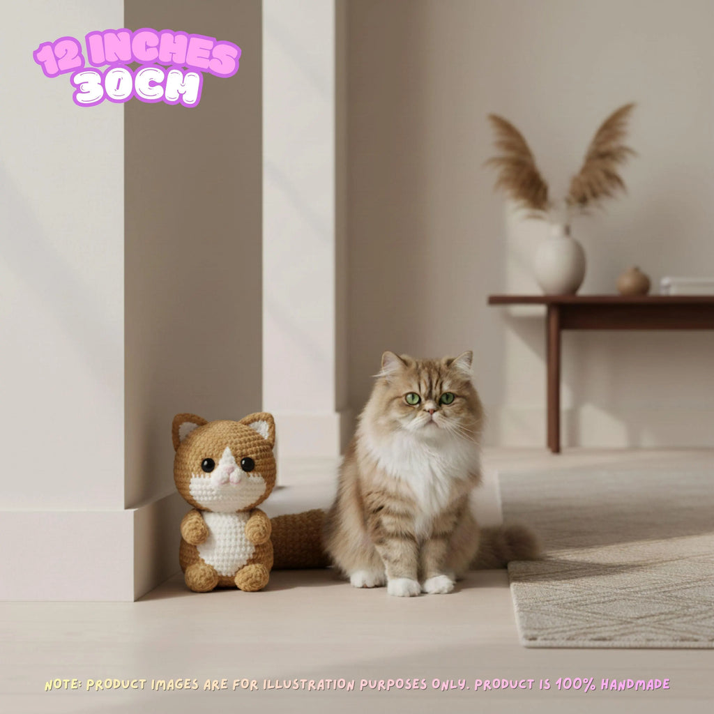 A fluffy long-haired cat sits beside a crocheted cat toy in a softly lit indoor room. Pink text in the top left reads '12 INCHES 30CM', and small disclaimer text appears along the bottom.