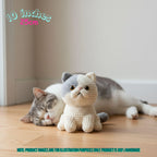 A crocheted cat plush toy sits on a wooden floor next to a sleeping gray-and-white cat in a home interior. Text in the top left reads '10 inches 25cm,' and a note at the bottom says product images are for illustration purposes only.