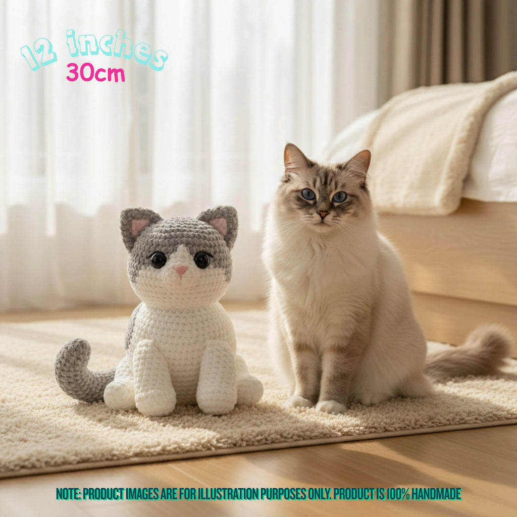 A crocheted plush cat toy sits on a beige rug beside a real cat in a softly lit bedroom. Text in the top left reads '12 inches 30cm,' and a note at the bottom says product images are for illustration purposes only because the product is 100% handmade.