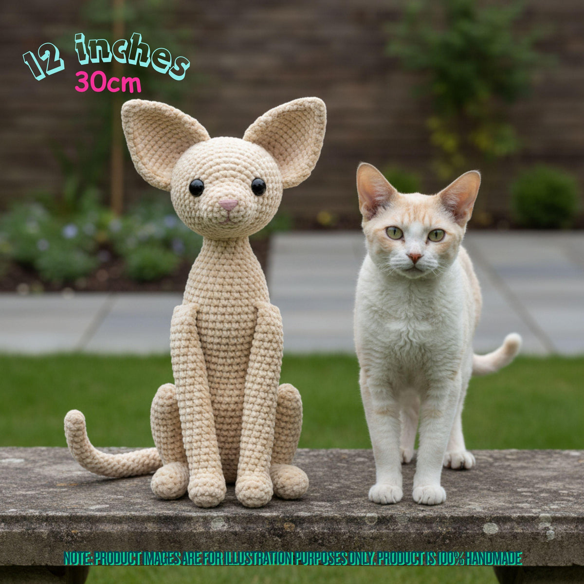 A crocheted cat-shaped plush toy sits on a stone ledge next to a real cat outdoors, with text in the top left reading '12 inches 30cm'. The toy is light cream/beige with black eyes and nose.