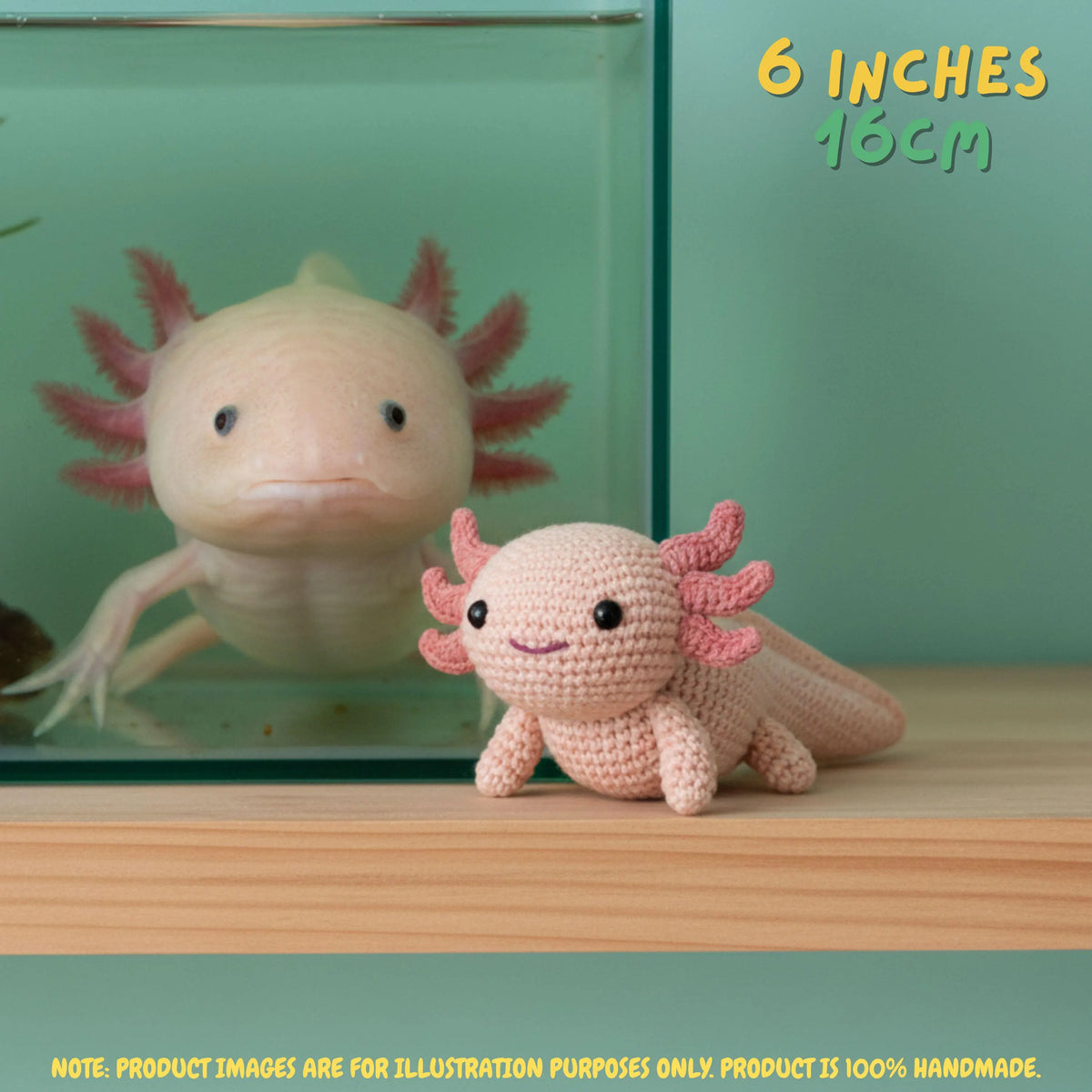 A crocheted axolotl toy in pale pink and coral pink is displayed on a wooden surface in front of a glass aquarium containing a real axolotl. Text in the top right reads '6 INCHES 15CM' and a note at the bottom says product images are for illustration purposes only.