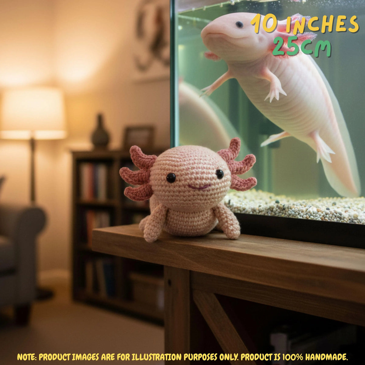 A crocheted axolotl toy sits on a wooden table in a cozy living room, with a real axolotl swimming in a fish tank behind it. Text overlays indicate the toy is 10 inches (25 cm) long, and a note at the bottom says the product image is for illustration purposes only and the product is 100% handmade.