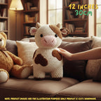 A crocheted cow plush toy sits on a brown sofa in a cozy living room, with a human hand touching its side. A teddy bear is partly visible on the left, and text in the top right reads '12 INCHES 30CM'.