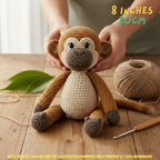 A crocheted plush monkey toy being held by two hands on a wooden table, with a ball of tan yarn, a crochet hook, and green leaves nearby. Text in the top right reads '8 INCHES 20CM' and a note at the bottom says product images are for illustration purposes only.