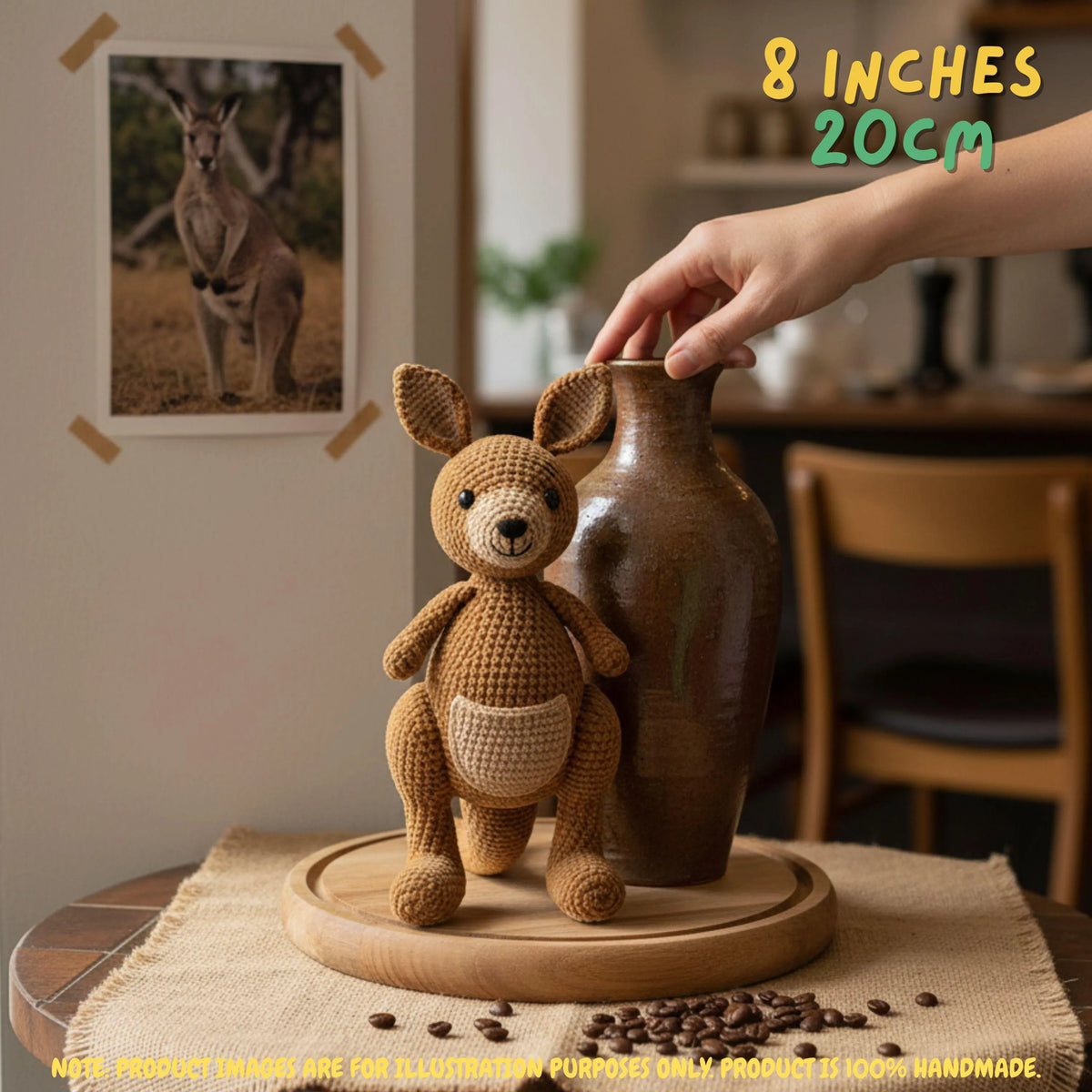 A crocheted kangaroo toy stands on a round wooden base beside a brown ceramic vase in a styled indoor setting. A human hand is touching the vase, and the scene includes overlaid text reading '8 INCHES 20CM' and a kangaroo photo on the wall.