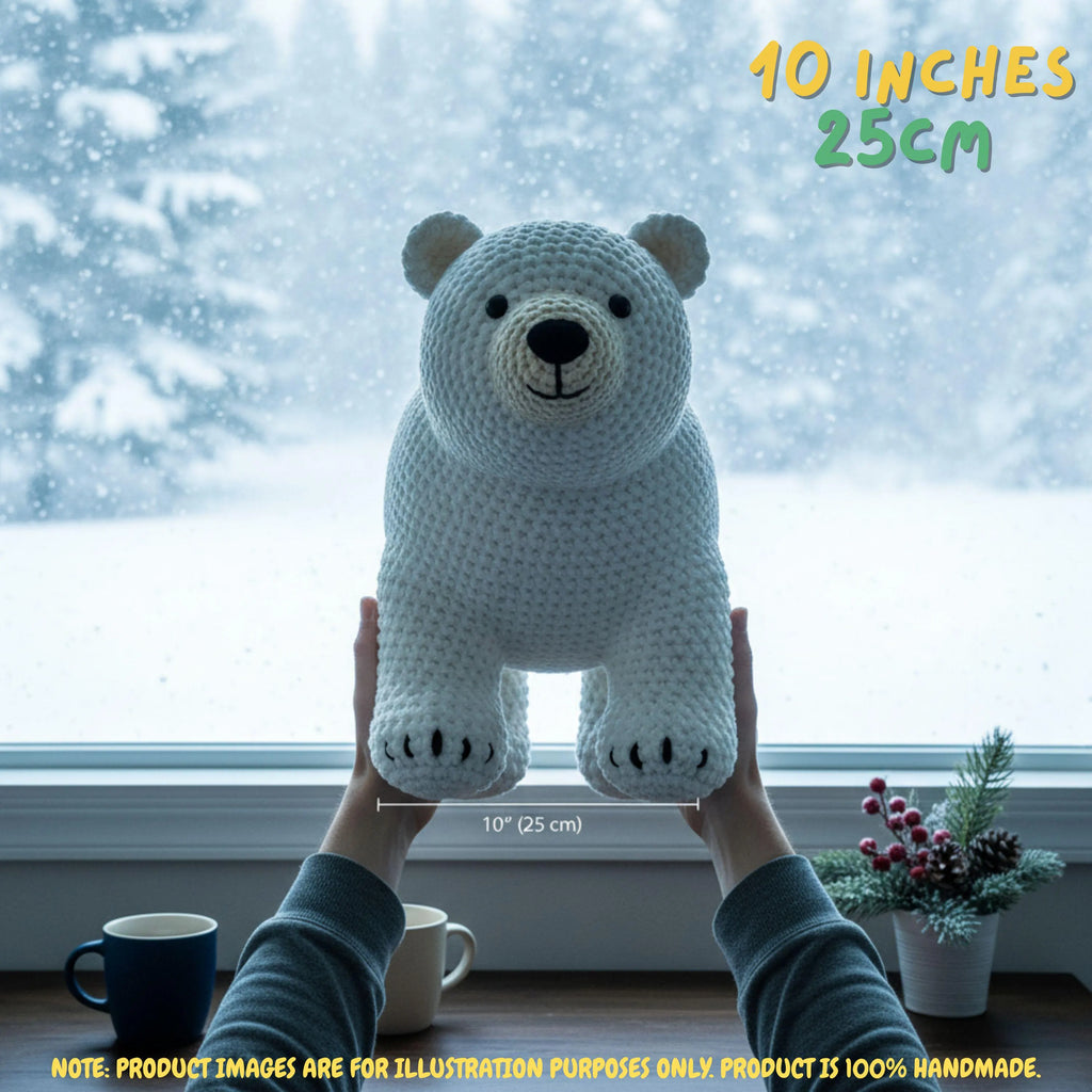 A crocheted polar bear toy is held up by two hands in front of a snowy window. The text '10 INCHES 25CM' and '10" (25 cm)' indicate the size of the plush toy.