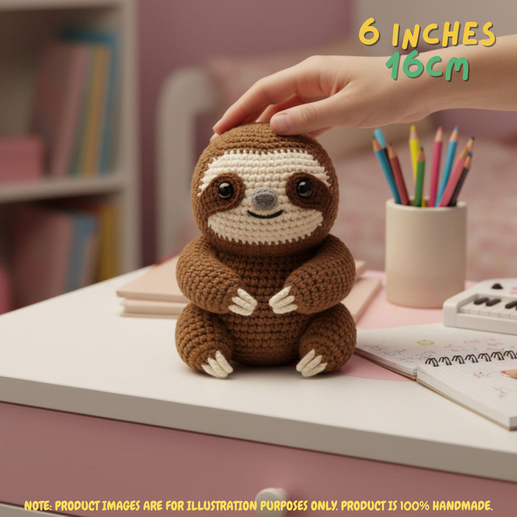 Handmade brown crochet sloth amigurumi doll sitting on a desk with a hand holding its head, featuring "6 INCHES / 16CM" text overlay.