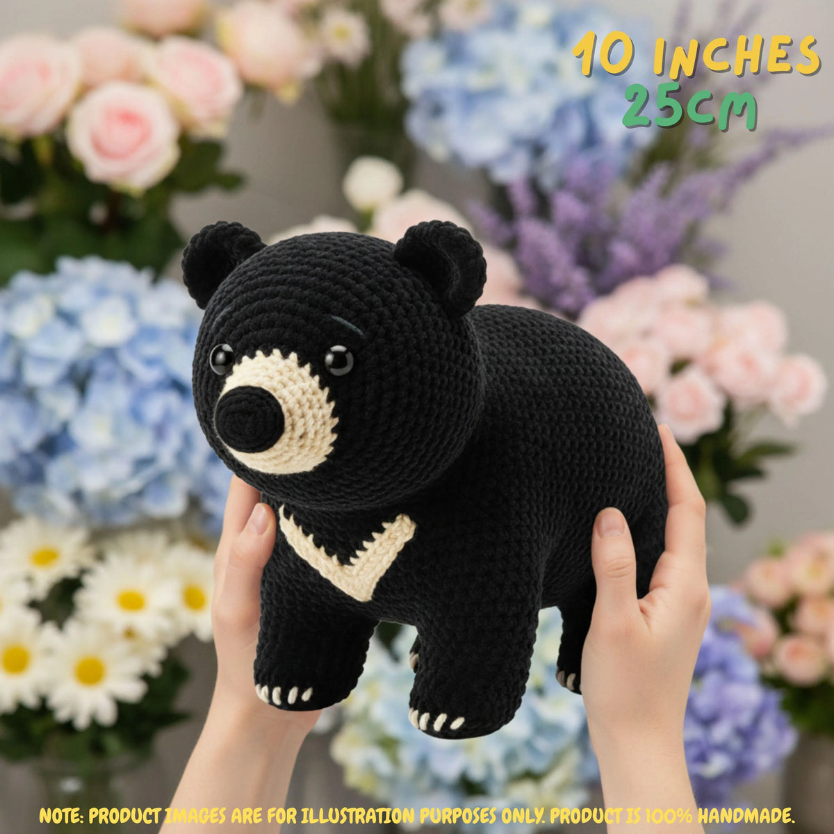 A crocheted black bear plush toy with cream-colored accents is being held up by two hands against a soft-focus background of pink, blue, and white flowers. Yellow text in the top right corner reads '40 INCHES 25CM', and a yellow note at the bottom states 'NOTE: PRODUCT SIZES ARE FOR ILLUSTRATION PURPOSES ONLY.