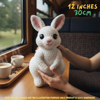A crocheted white bunny plush toy with pink inner ears and black eyes, being held by hands on a wooden table by a window. Text in the top right reads '12 INCHES 30cm'.