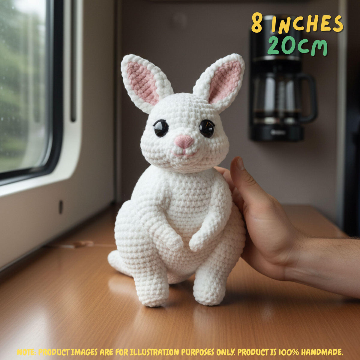 A white crocheted bunny plush toy with pink inner ears is shown on a wooden surface next to a window, with a human hand supporting it. Text in the top right reads '8 INCHES 20cm', and a note at the bottom says product images are for illustration purposes only.