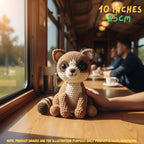 Handmade Ringtail crochet amigurumi plush doll with a striped tail resting on a wooden table held gently by a hand, in a train car setting with text indicating 10 inches 25 cm size.