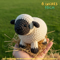 Crocheted amigurumi sheep toy held in a person's hand on a bed of straw, with a green grassy background and text reading '6 INCHES 16CM'.