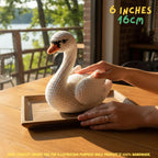 Handmade Mute Swan crochet amigurumi plush doll in white with an orange beak, resting on a woven mat in a nursery room setting.