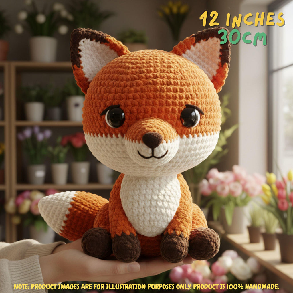 A crocheted fox plush toy being held in a person's hand, with a blurred indoor flower shop background. Text overlays read '12 INCHES 30CM' and note that the product is 100% handmade.