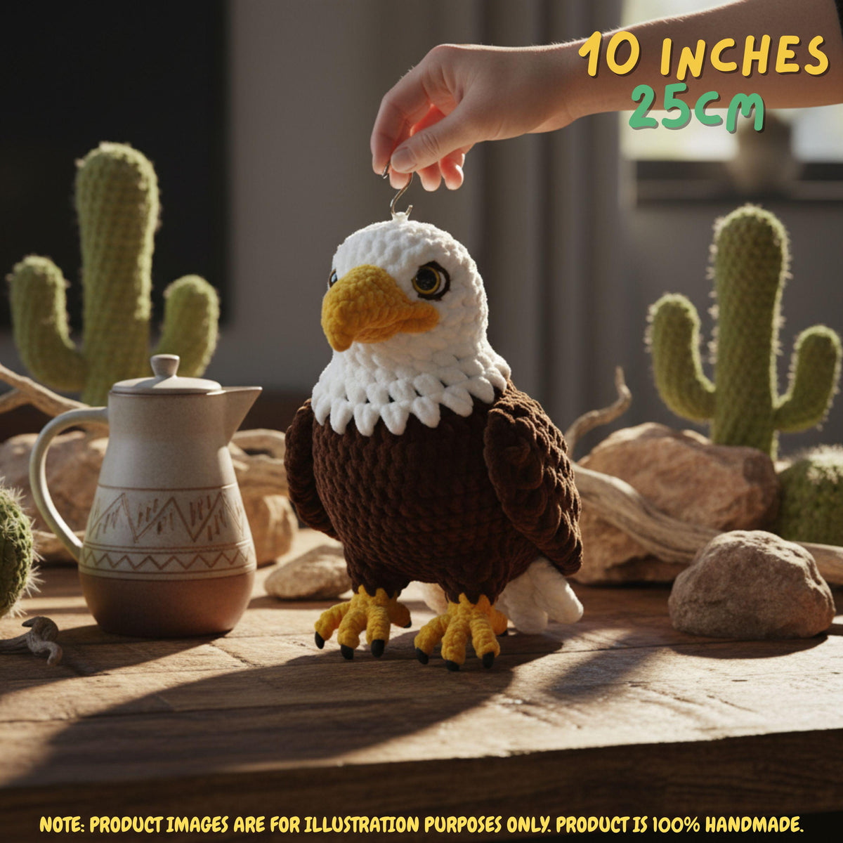 A hand is holding the top of a crocheted bald eagle ornament or figurine on a rustic wooden surface, with cacti, rocks, and a small teapot in the background. Text in the top right reads '10 INCHES 25CM' and a note at the bottom says product images are for illustration purposes only.