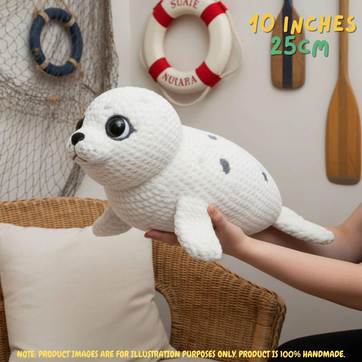 A white crocheted seal plush toy being held by a person's hands in a nautical-themed room setting. The plush has black eyes, a black nose, and small black spots.