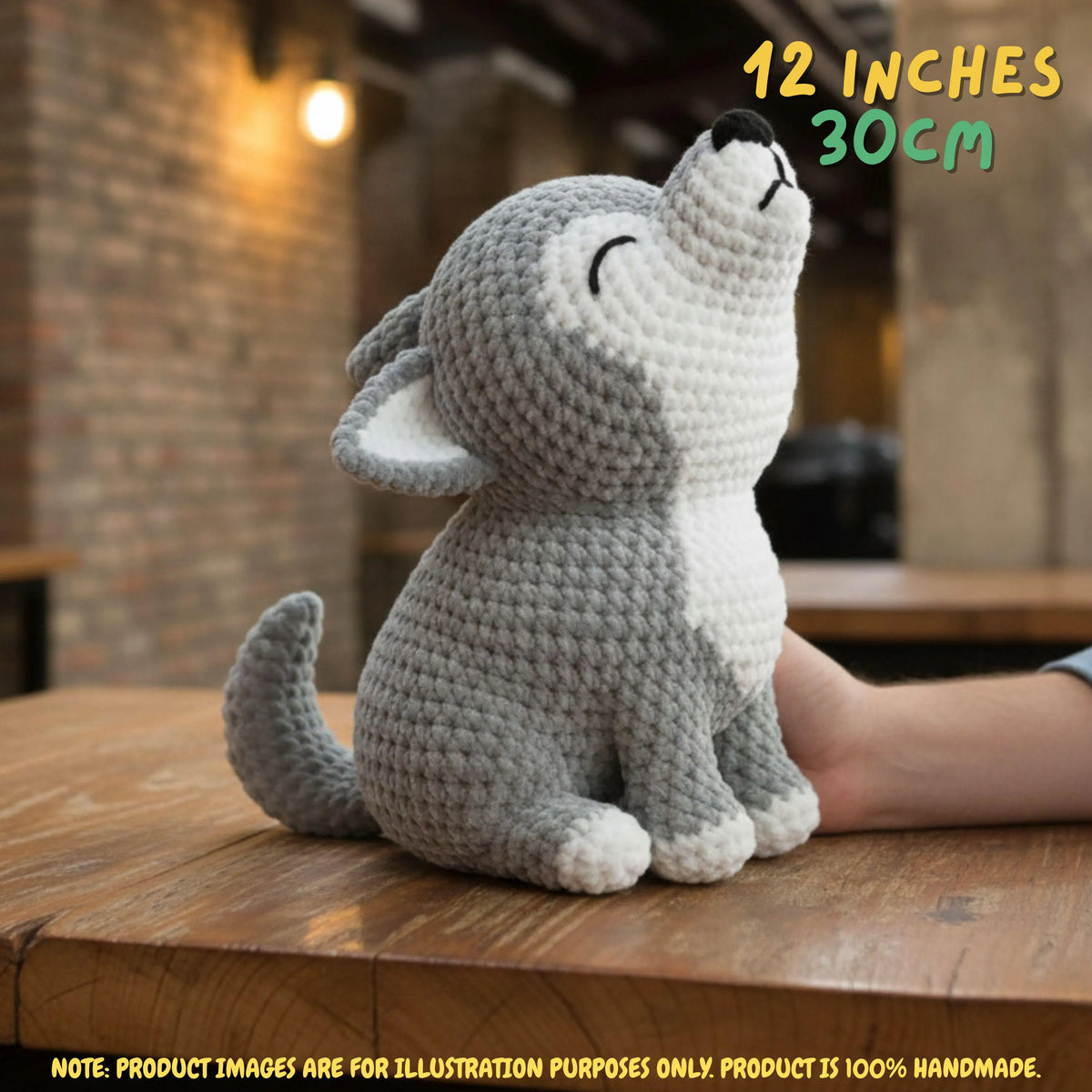 Handmade grey and white crochet wolf amigurumi doll in a howling pose sitting on a wooden table with a hand resting near it, featuring "12 INCHES / 30CM" text overlay.