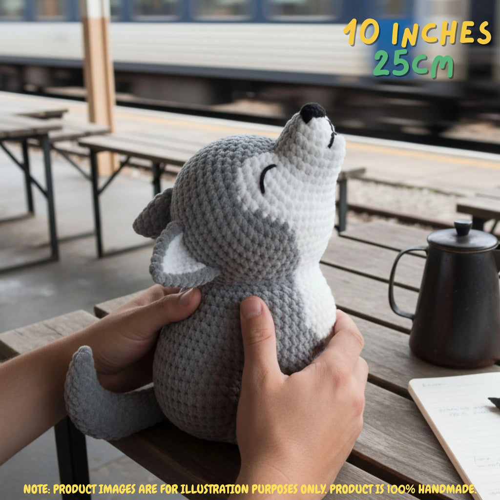 Handmade grey and white crochet wolf amigurumi doll in a howling pose held by hands on a wooden outdoor bench, featuring "10 INCHES / 25CM" text overlay.