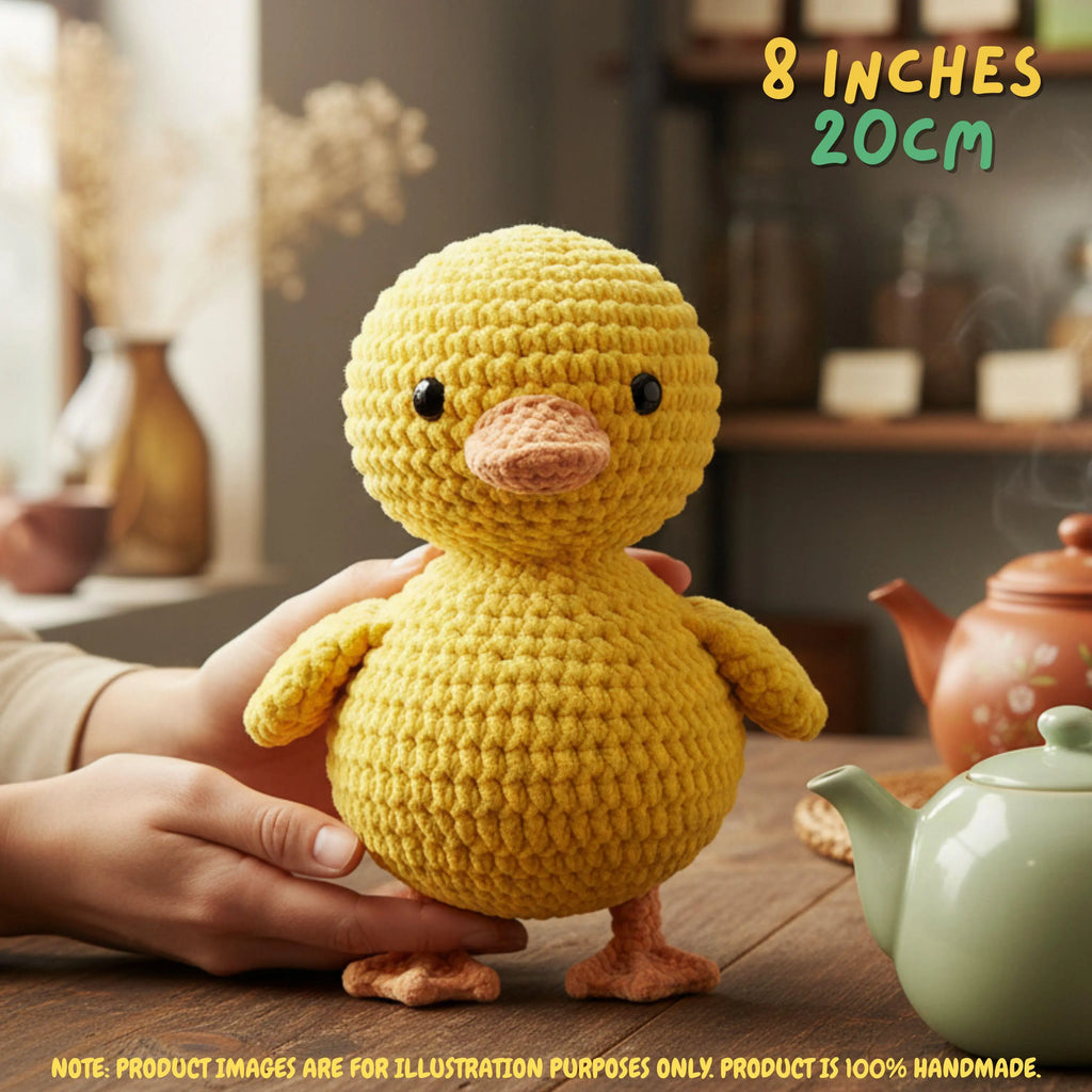 A yellow crocheted duck toy being held by hands on a wooden table, with a teapot in the background and text overlays reading '8 INCHES 20CM' and 'NOTE: PRODUCT IMAGES ARE FOR ILLUSTRATION PURPOSES ONLY. PRODUCT IS 100% HANDMADE.
