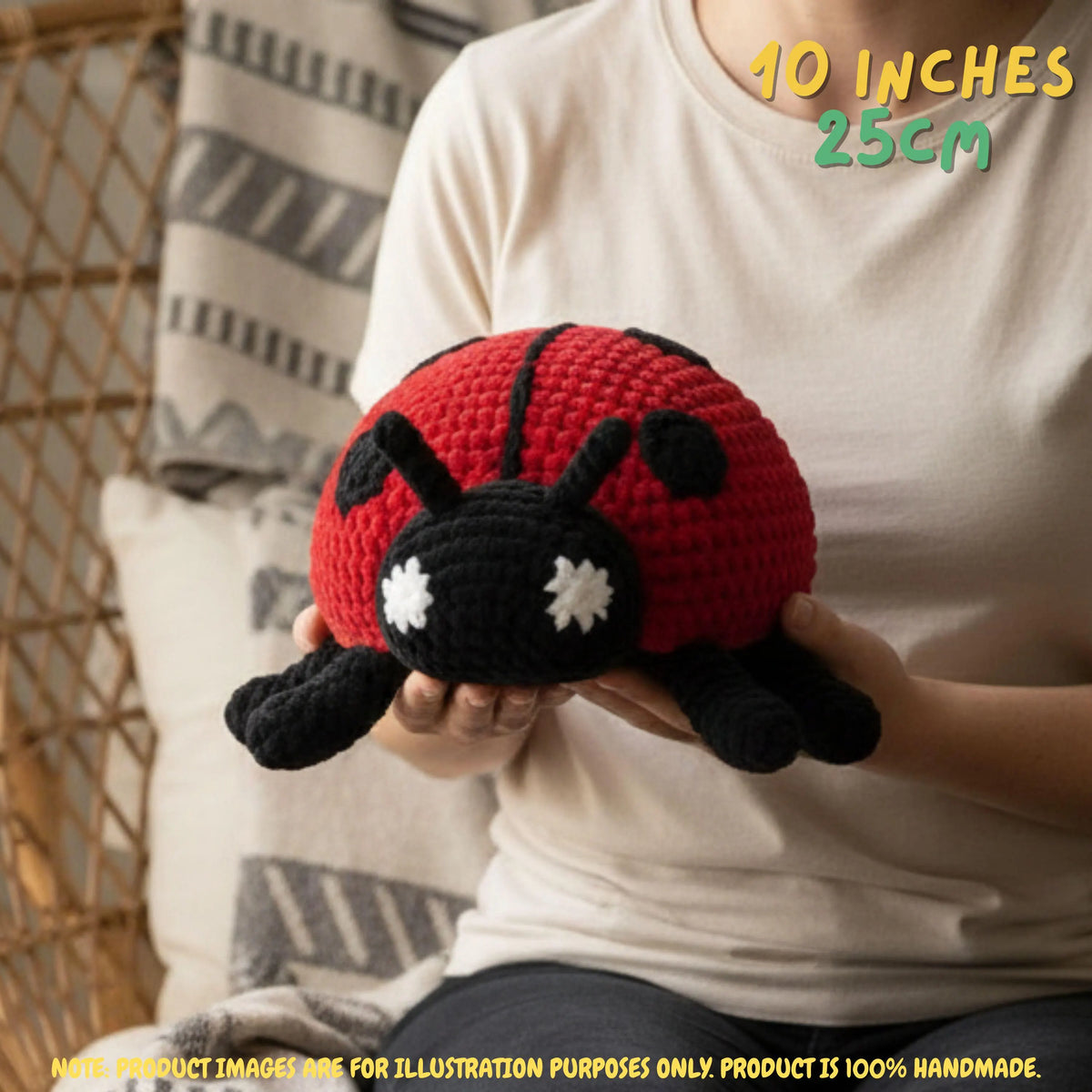 A person in a white t-shirt holds a crocheted ladybug toy. The toy has a red body with black spots, black legs and head, and white embroidered eyes.