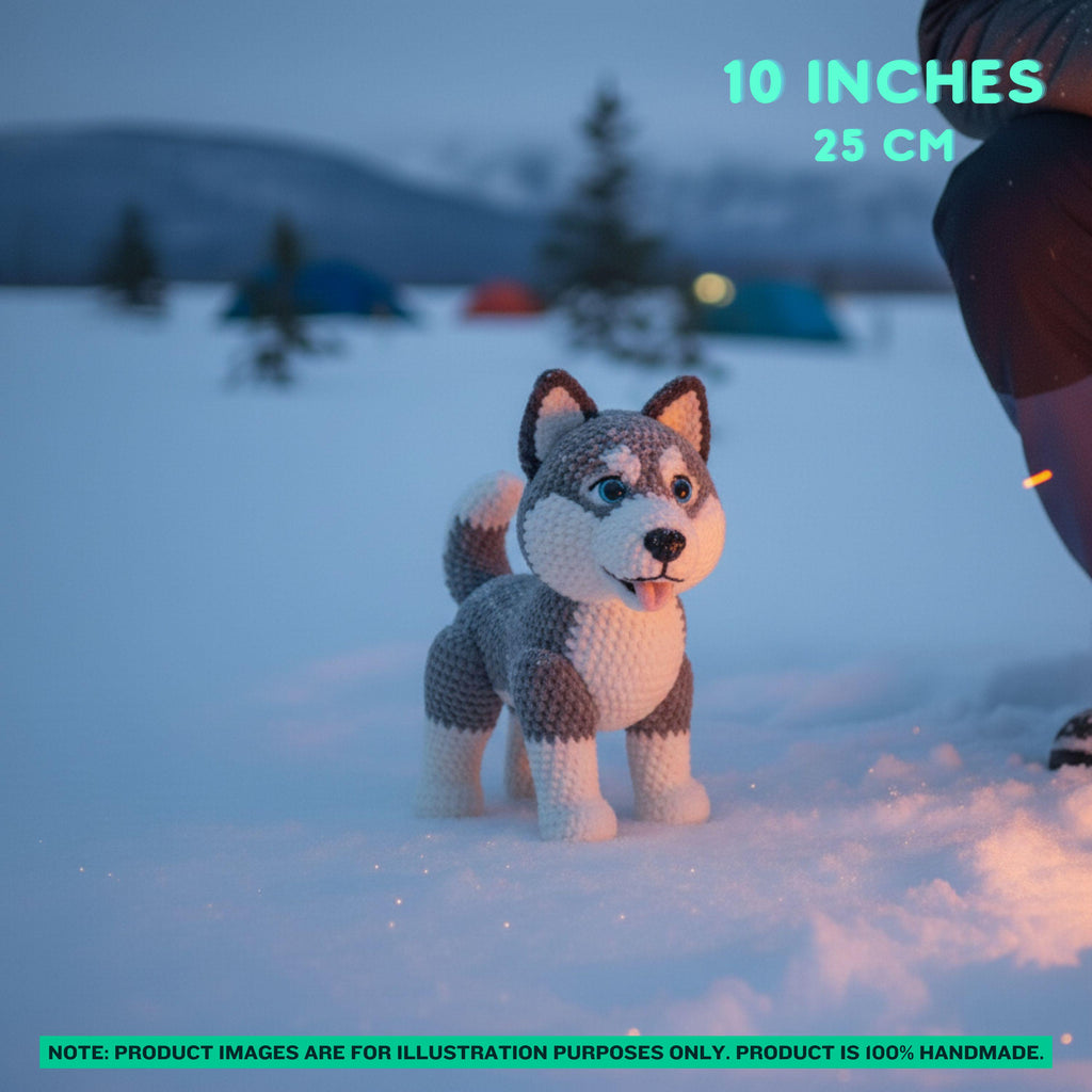 A crocheted plush dog toy standing in snow, with a blurred winter outdoor scene in the background. Text overlays read '10 INCHES 25 CM' and a note at the bottom says product images are for illustration purposes only.
